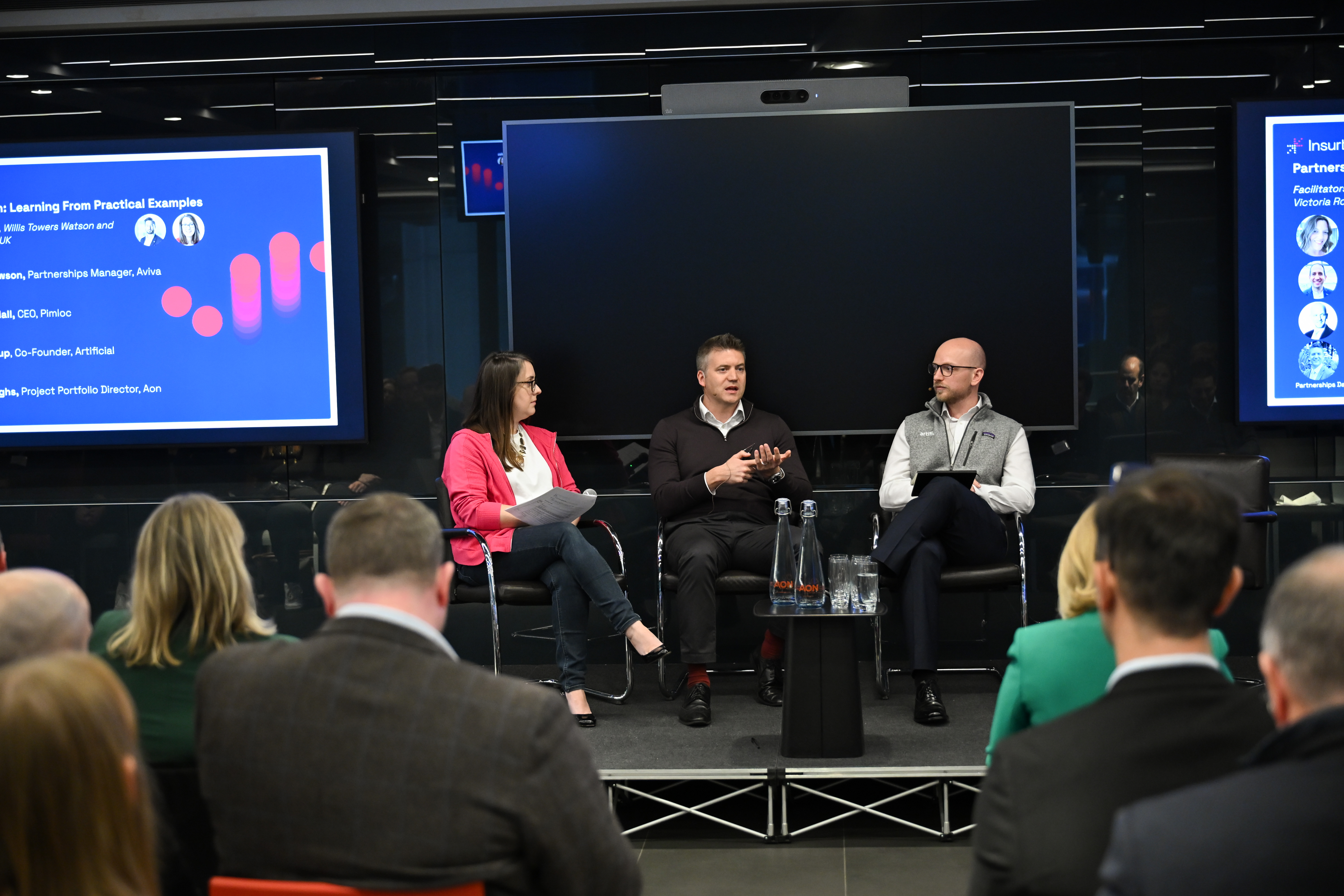 Woman in red jacket sitting on stage talking with two men