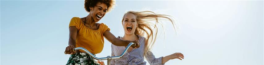 Two girls playing with a bicycle on the boardwalk on a seaside holiday.